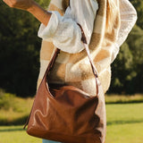 Person holding a brown leather bag outdoors in a natural setting