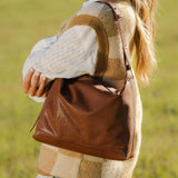 Person wearing a plaid sweater and holding a brown leather bag in a grassy field