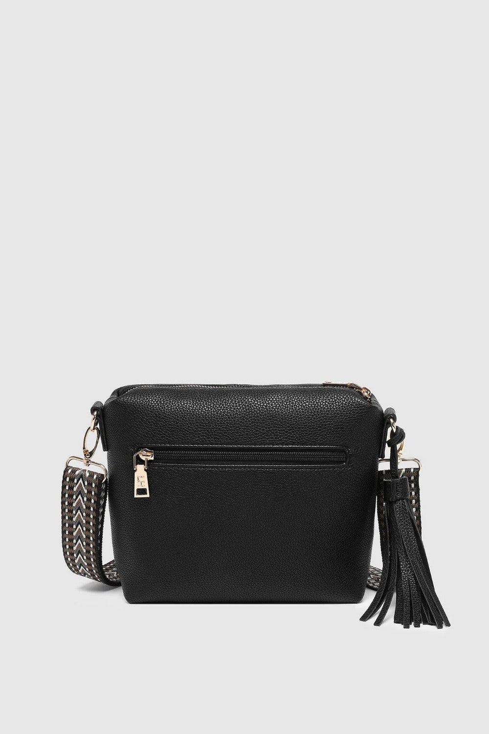 A black pebbled faux-leather crossbody bag with an external zip pocket, a woven strap detail, and a black tassel charm, shown against a light gray background.