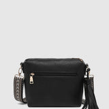 A black pebbled faux-leather crossbody bag with an external zip pocket, a woven strap detail, and a black tassel charm, shown against a light gray background.