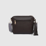 A dark brown textured faux-leather crossbody bag with a patterned strap and a tassel accent, shown against a light gray background.