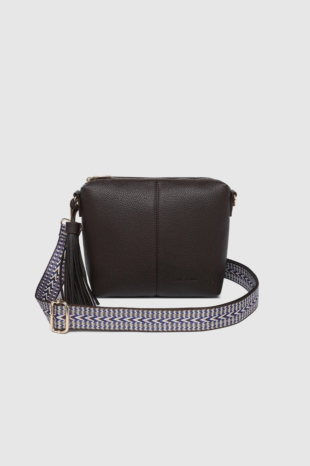 A dark brown pebbled leather crossbody bag with a patterned woven strap featuring a tassel detail and silver-tone hardware, shown against a light gray background.