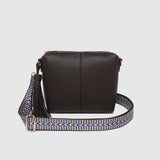 A dark brown pebbled leather crossbody bag with a patterned woven strap featuring a tassel detail and silver-tone hardware, shown against a light gray background.