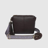 A dark brown pebbled pleather crossbody bag with a patterned woven strap, a separate thinner pleather strap, and gold-tone hardware, shown against a light gray background.