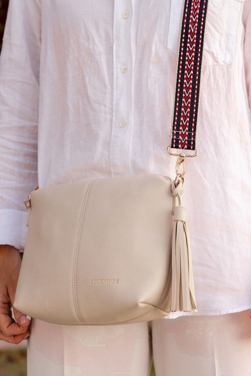 Beige handbag with a tassel held by a person wearing a white shirt.