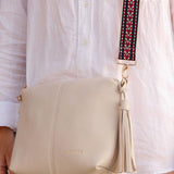 Beige handbag with a tassel held by a person wearing a white shirt.