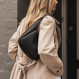 Woman in a beige trench coat with a black bag walking past a door.