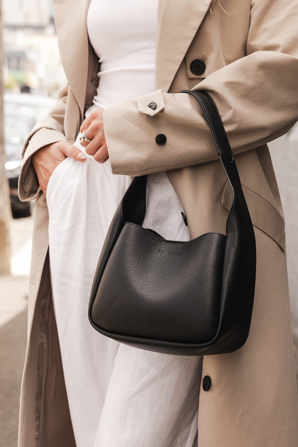 Person wearing a beige coat holding a black handbag.