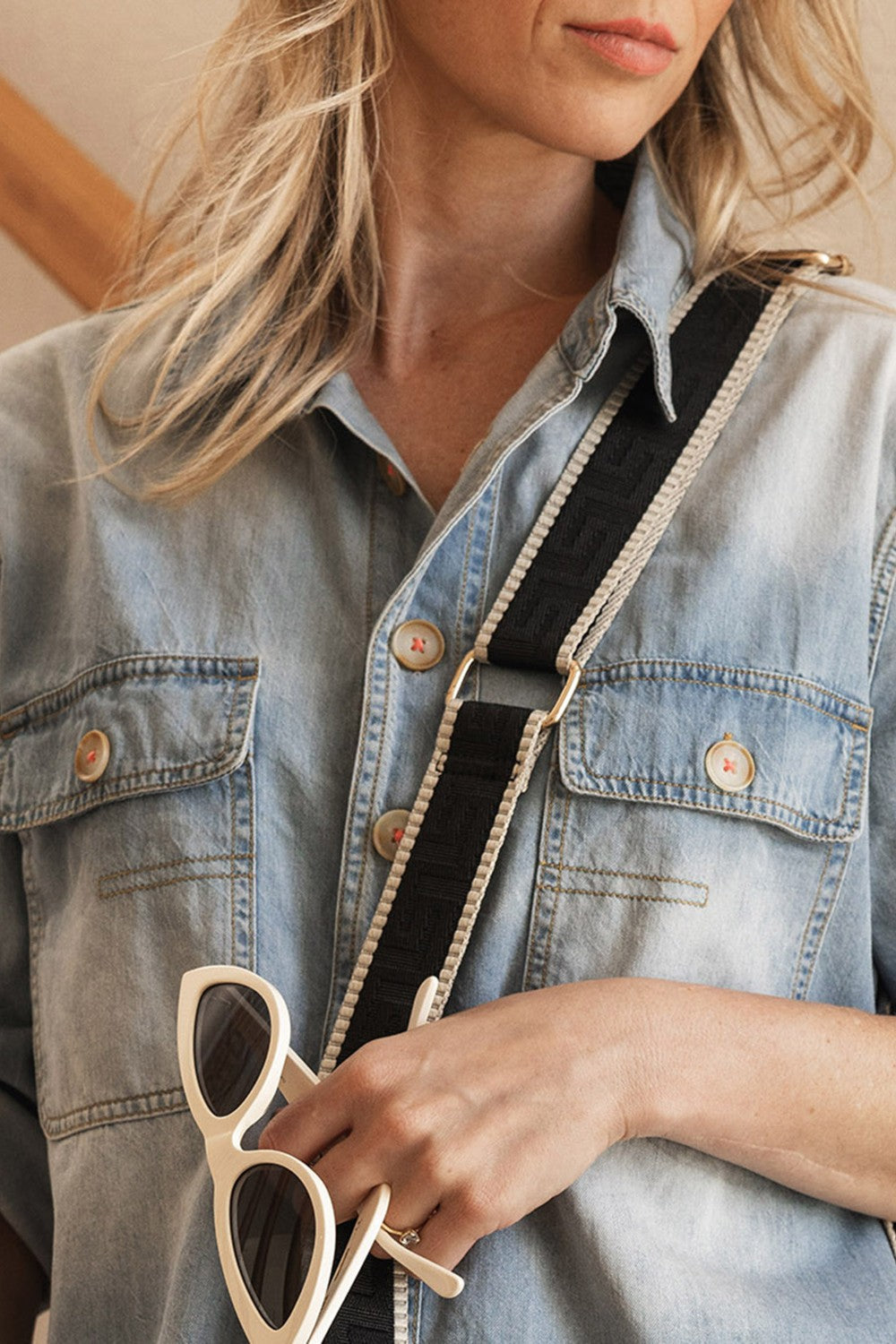Person wearing a denim jacket holding sunglasses with a neutral background