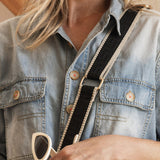 Person wearing a denim jacket holding sunglasses with a neutral background