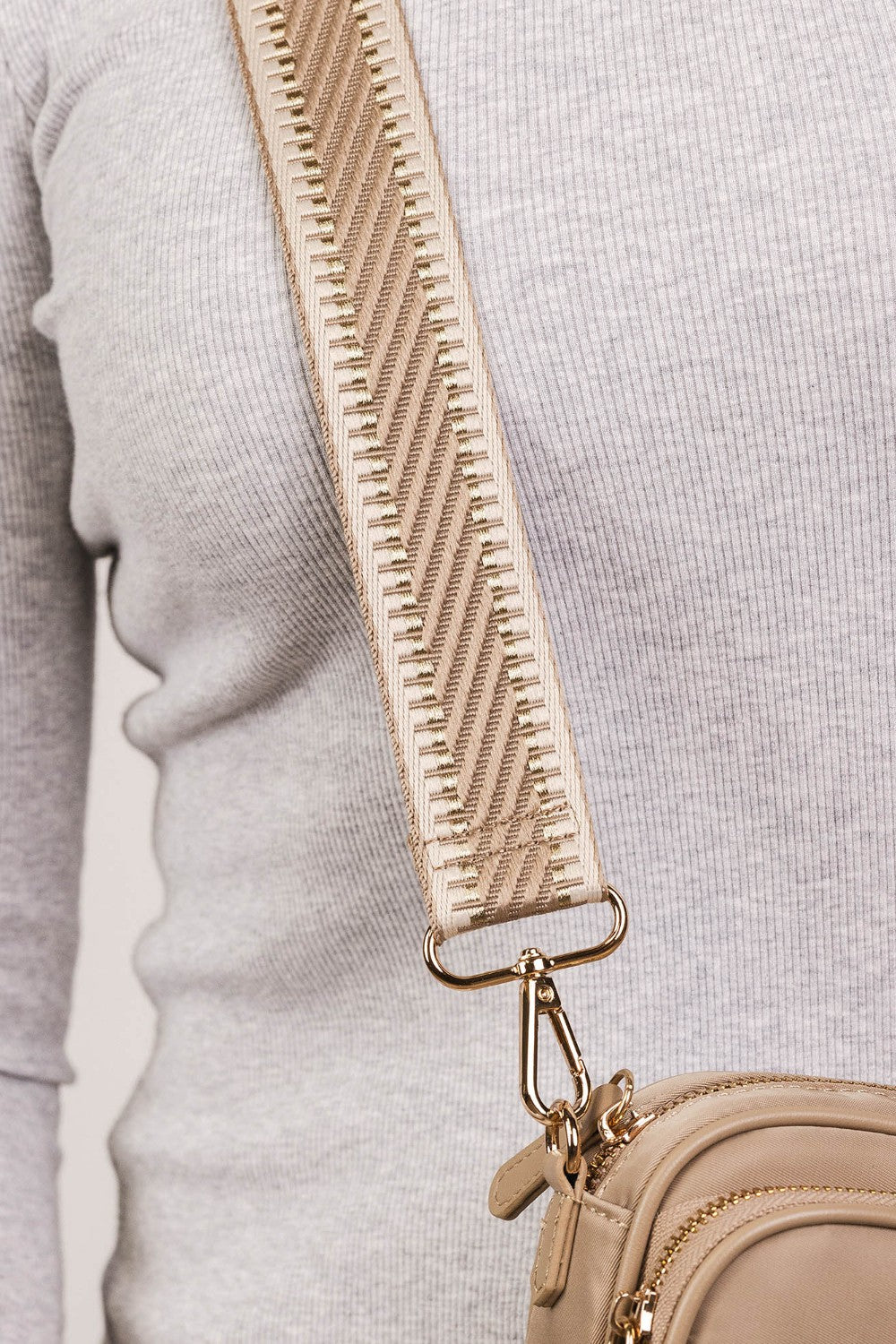 Beige crossbody bag with textured strap on a light gray background