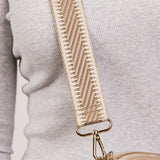 Beige crossbody bag with textured strap on a light gray background