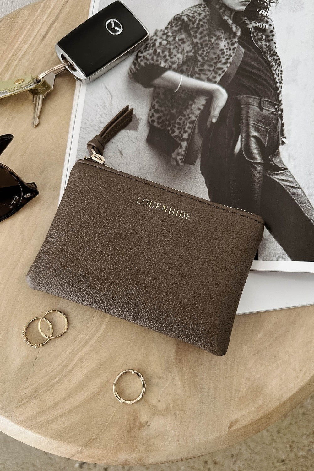 Brown pleather pouch with 'LOUENHIDE' branding on a wooden surface with keys and rings.