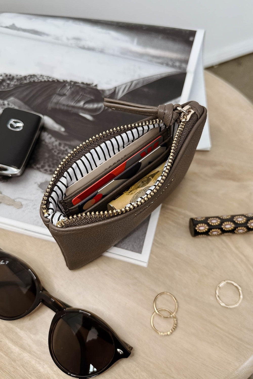 Brown zippered pouch with sunglasses and jewelry on a wooden surface