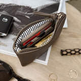 Brown zippered pouch with sunglasses and jewelry on a wooden surface