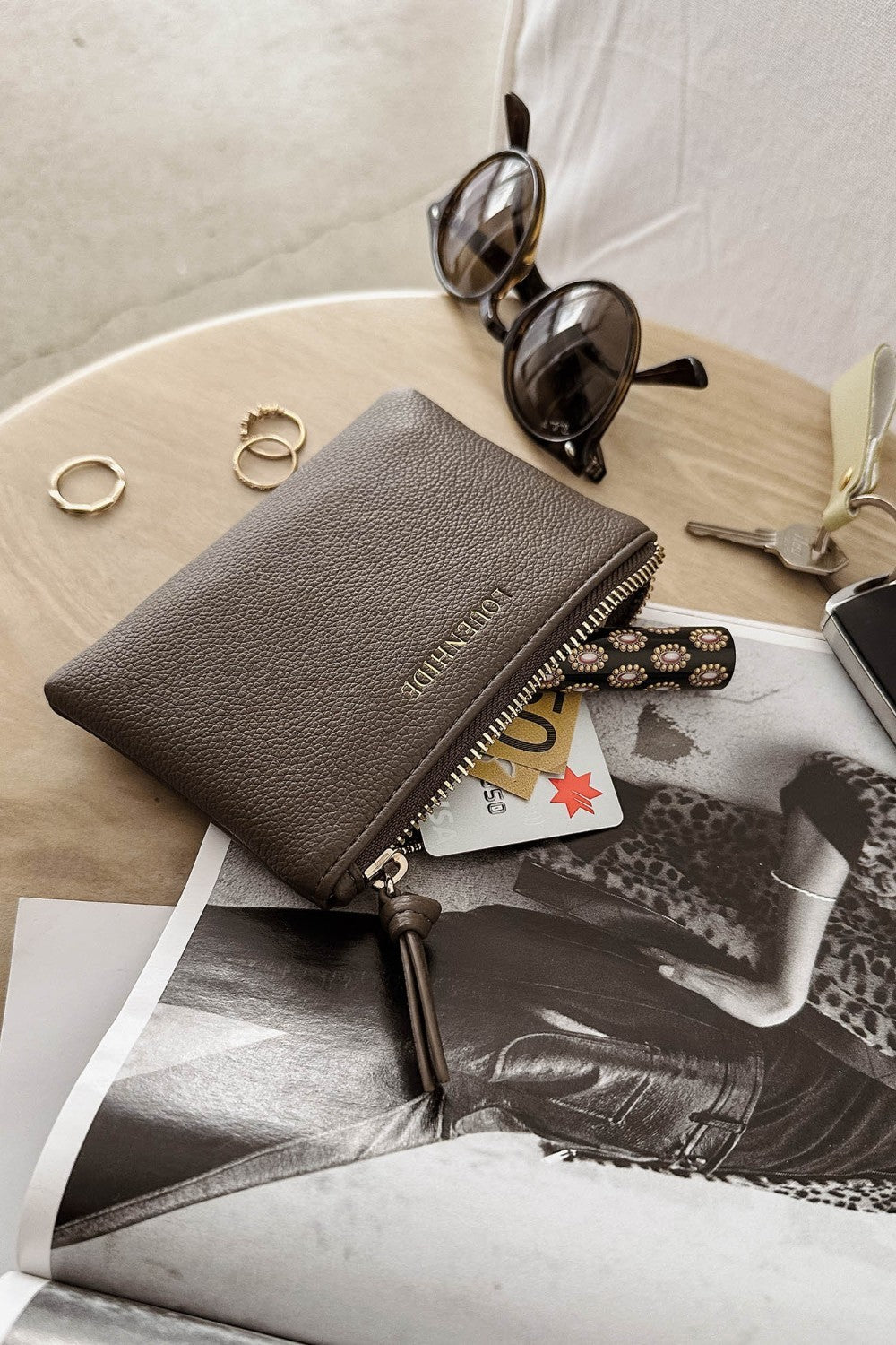 Brown pleather wallet with sunglasses, keys, and cards on a magazine
