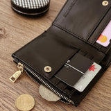A black leather bifold wallet shown open on a wooden tabletop, with cards, coins, and a small round compact nearby. The wallet has gold-tone hardware and a visible interior embossed LOUENHIDE logo.