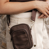 Brown crossbody bag worn over shoulder with stone wall background