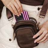 Person holding a brown crossbody bag with a striped phone case.