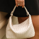 Person holding a woven handbag with a neutral background