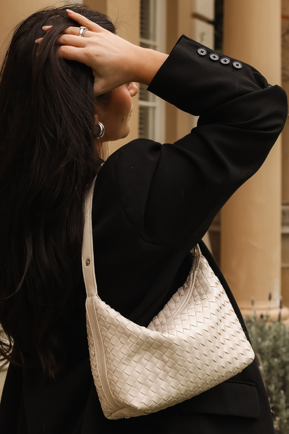 Person wearing a black coat with a white woven handbag, outdoors.