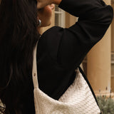Person wearing a black coat with a white woven handbag, outdoors.