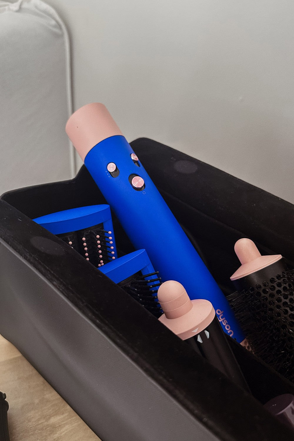 Blue hair straightener with pink handles on a black stand against a neutral background