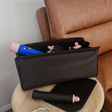 Black travel case with makeup items on a wooden side table next to a brown leather sofa.