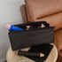 Black travel case with makeup items on a wooden side table next to a brown leather sofa.