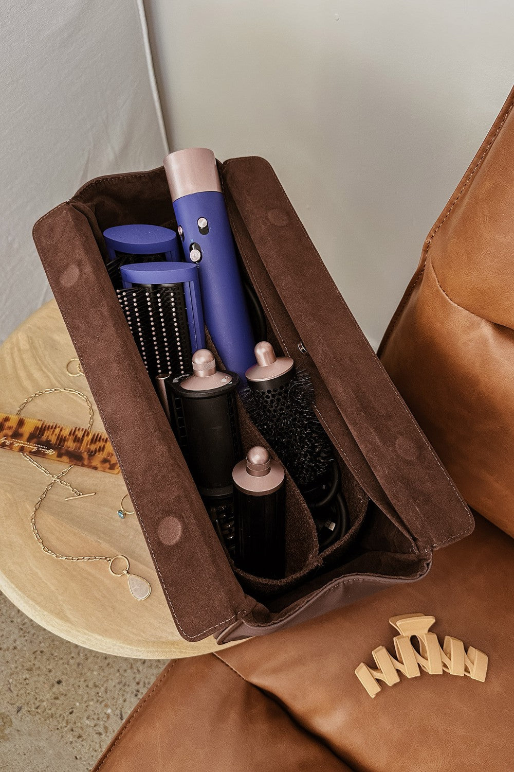 Set of hair styling tools in a brown pleather case on a wooden surface.