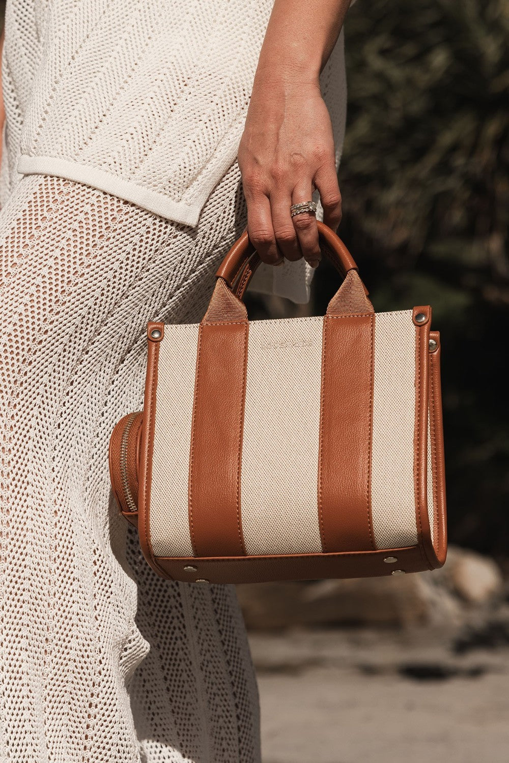 Person holding a striped handbag with brown leather accents