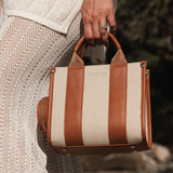Person holding a striped handbag with brown leather accents