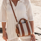 Woman holding a striped handbag on a beach