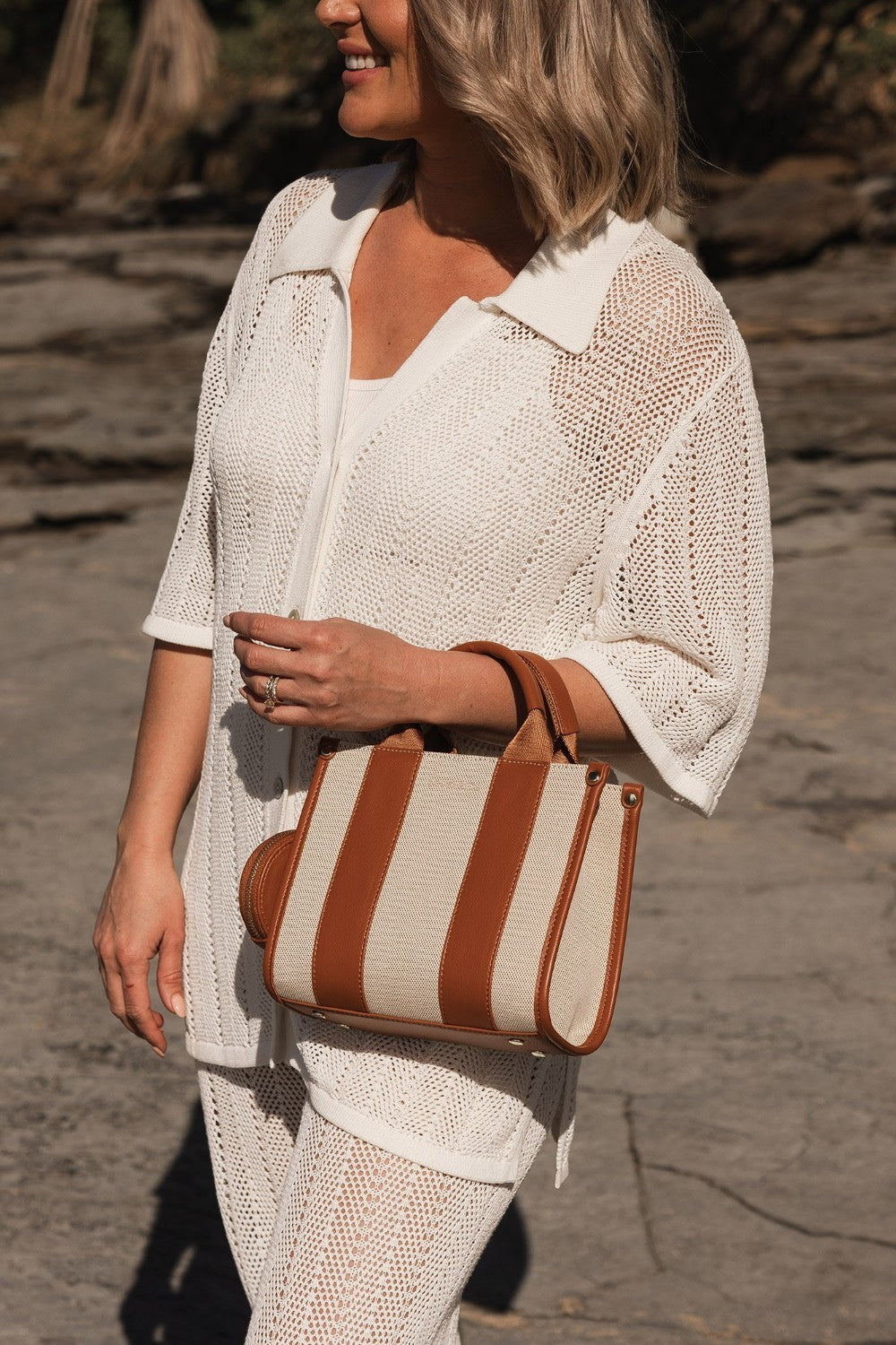 Woman holding a brown and beige striped bag on a rocky surface
