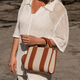 Woman holding a brown and beige striped bag on a rocky surface