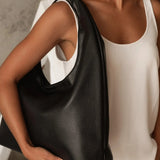 A woman wearing a white sleeveless top carries a large black pebbled leather shoulder bag with a wide integrated shoulder strap.
