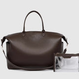 A large brown pebbled leather duffel bag with handles and a detachable strap with a clear pouch on a light background.