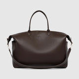 A large brown pebbled leather duffel bag with handles and a detachable strap on a light background.