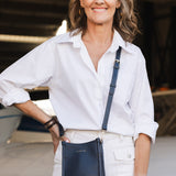 Woman in a white shirt and pants holding a navy blue bag, standing in front of an airplane.