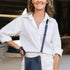 A woman wearing a white button-down shirt and white pants carries a navy blue leather crossbody bag with a matching strap in a boat garage setting.
