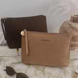 Two small zip pouches with wrist straps are displayed on a marble surface. The front pouch is tan and labeled LOUENHIDE, while the pouch behind it is dark brown.
