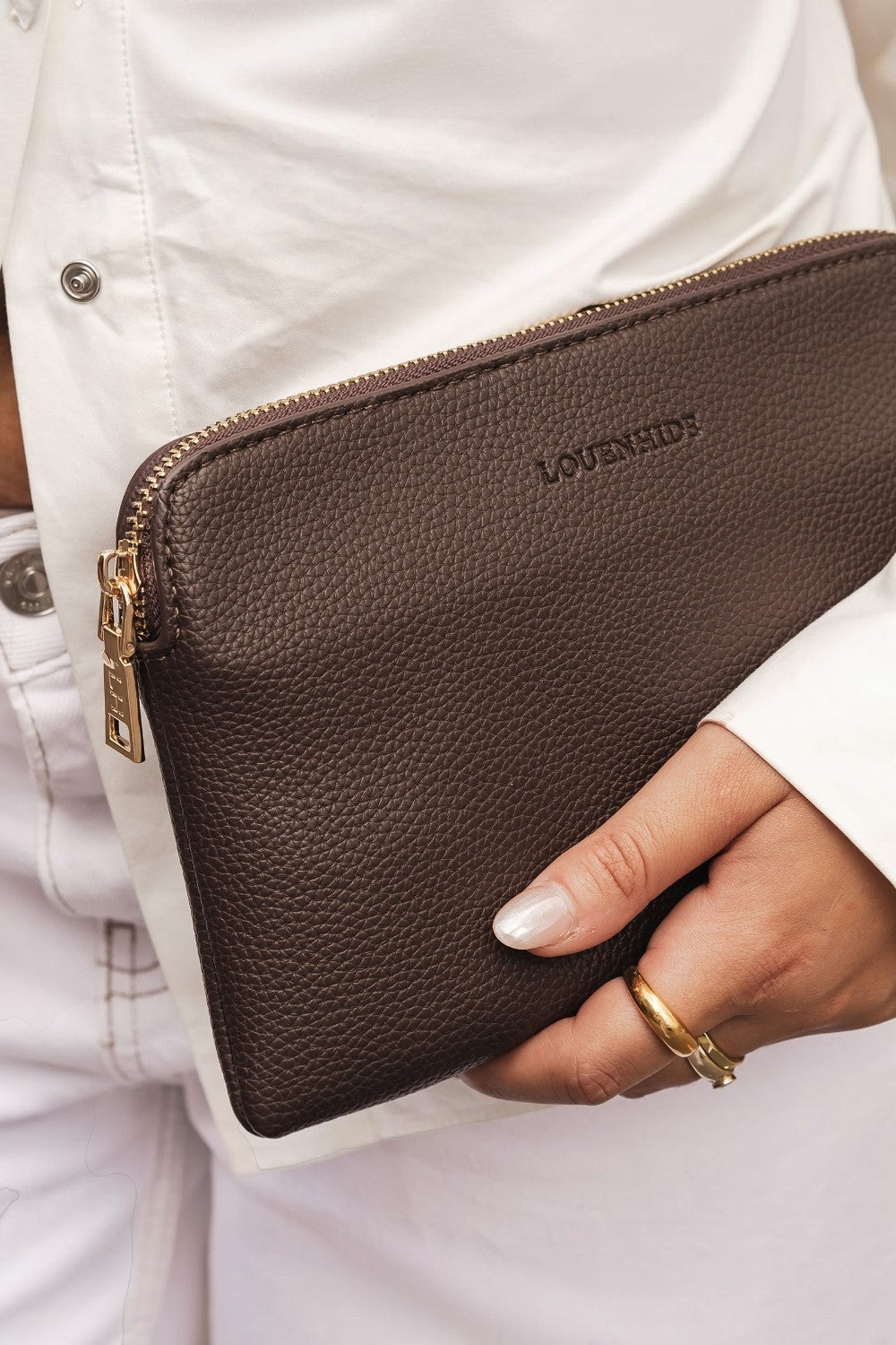 Brown leather clutch bag with gold zipper held by a person wearing a white jacket.