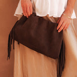 Brown clutch bag with fringes held by a person wearing a white top and beige skirt.