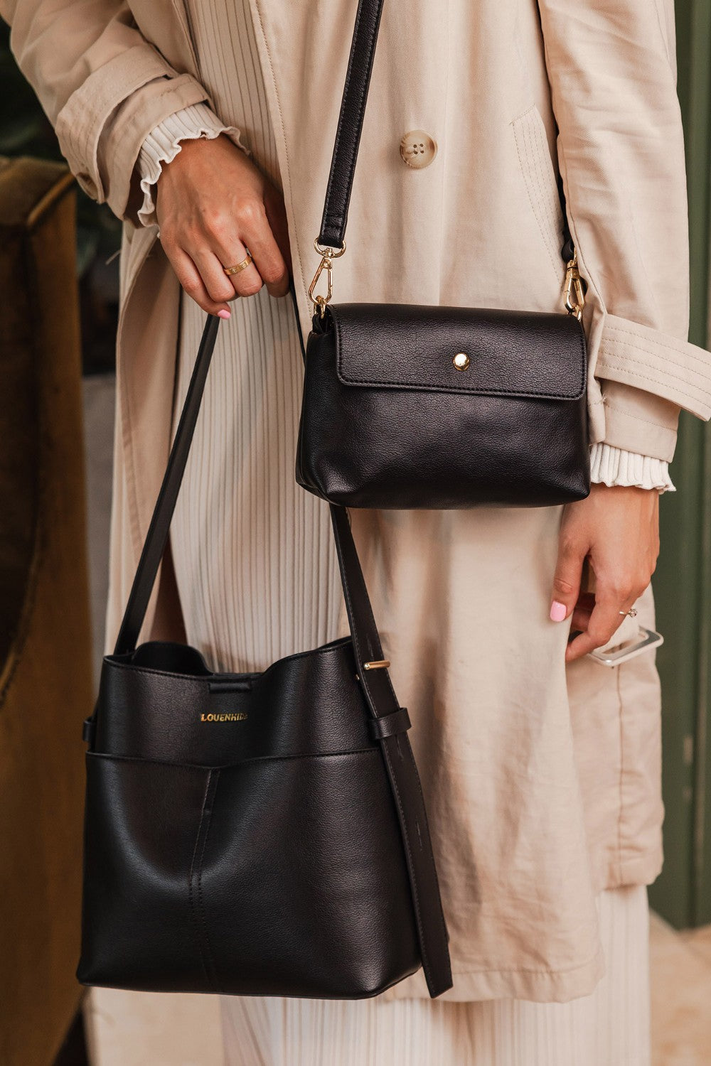 Person holding two black handbags, one in each hand, with a blurred background.