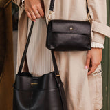 Person holding two black handbags, one in each hand, with a blurred background.