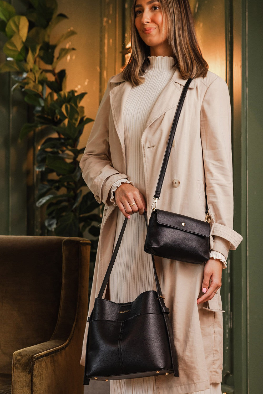 Woman holding two black handbags against a blurred indoor background