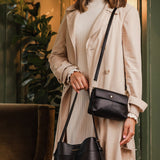 Woman holding two black handbags against a blurred indoor background