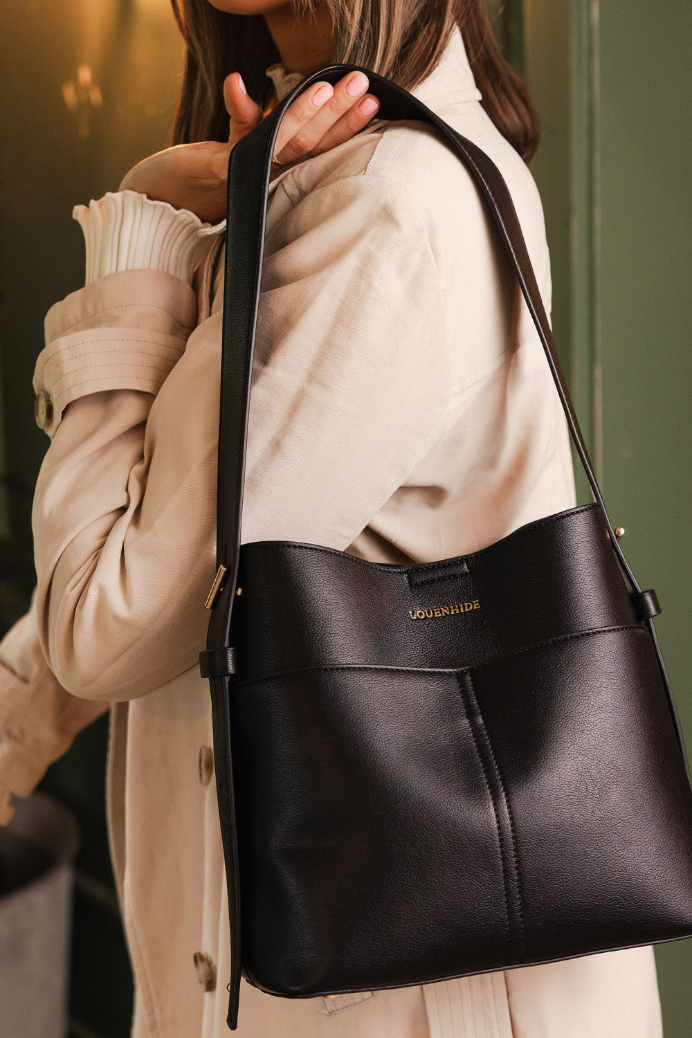 Person holding a black handbag with a visible brand name, wearing a beige coat.