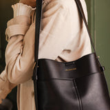 Person holding a black handbag with a visible brand name, wearing a beige coat.