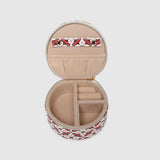 A round zippered jewellery case with a red, black, and white geometric pattern, shown against a solid light gray background.